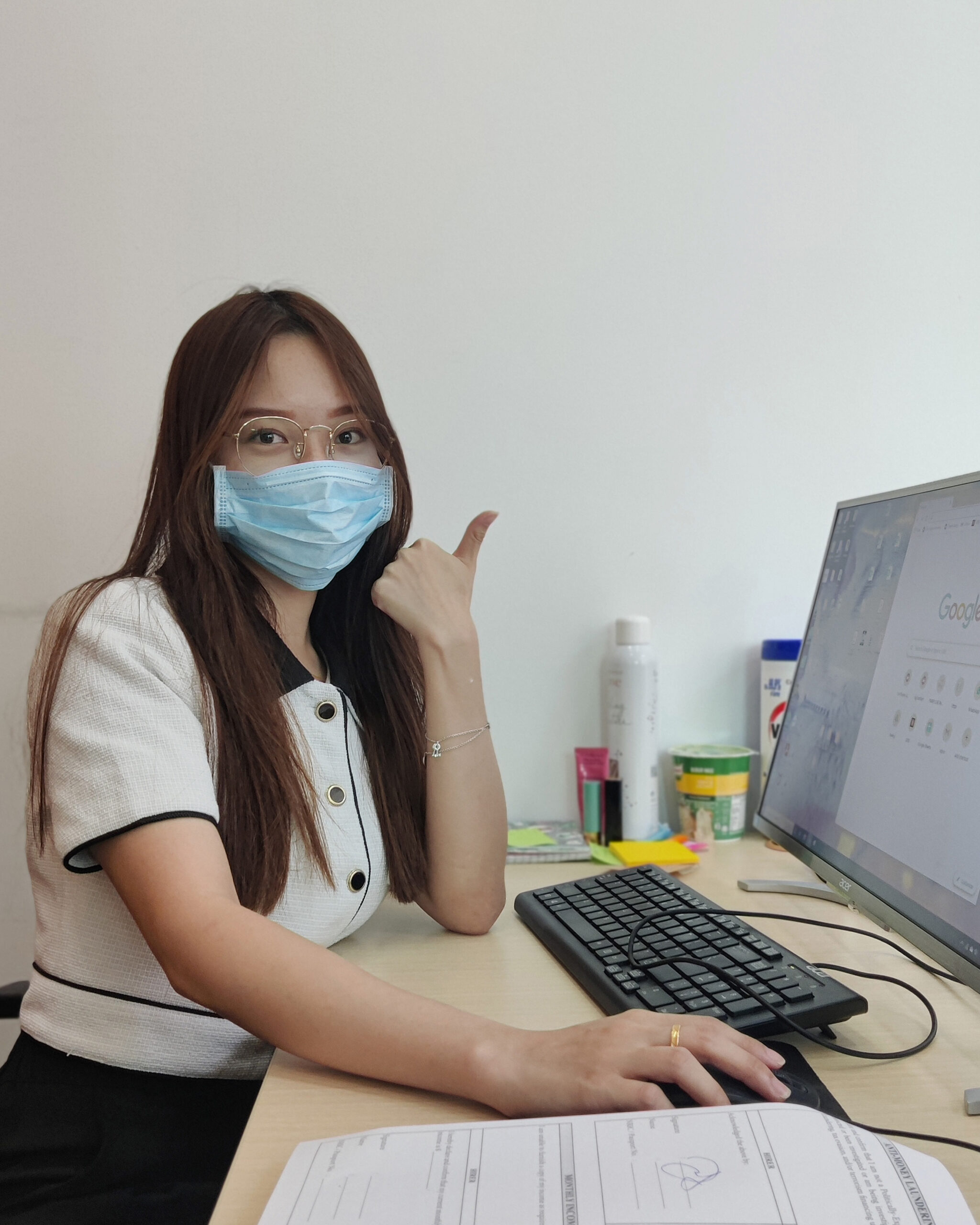 Satisfied PCExperts101 client wearing a face mask and giving a thumbs up while at a computer workstation, indicating successful PC support or service.